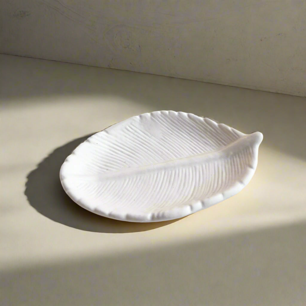 A white, leaf-shaped tray made of mineral powder known as Jesmonite, displayed on a sunny surface